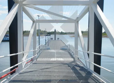 Passerelle métallique au platelage en caillebotis électroforgés, au-dessus d’un plan d’eau.